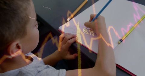 Young boy writing in notebook while holding pencil with financial chart overlay