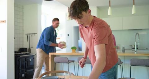 Teenager arranging table with father in modern open-plan kitchen preparing family meal