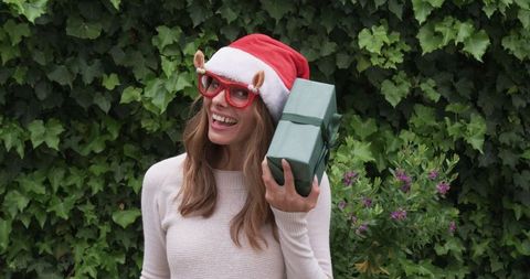 Festive woman joyfully holding wrapped gift in garden