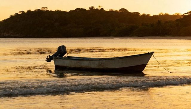 Weathered fishing skiff floating in golden sunset water, moored near tropical shoreline