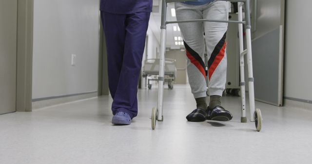 Elderly patient using a walker, guided by a caregiver, walking down a hospital corridor. This image is ideal for articles on healthcare, patient care, elderly support, physical rehabilitation, medical assistance, and hospital facilities.