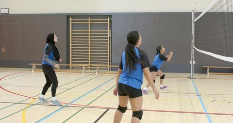 Diverse female volleyball team practicing indoors with hijab athlete and ready pass