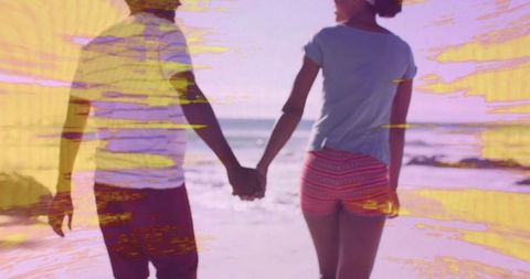 Couple holding hands walking along vibrant beachfront