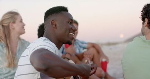 Young Man Playing Guitar with Friends at Beach Sunset