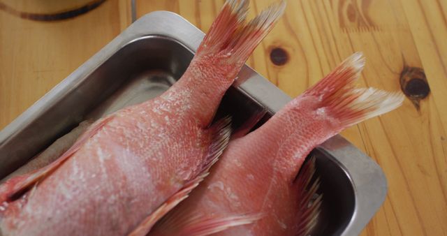 This image shows the tails of fresh red snapper fish resting in a metal tray on a wooden table. Ideal for use in culinary blogs, recipe sites, and health food promotions. Could be used to illustrate fresh seafood availability in restaurant menus or local market advertisements.