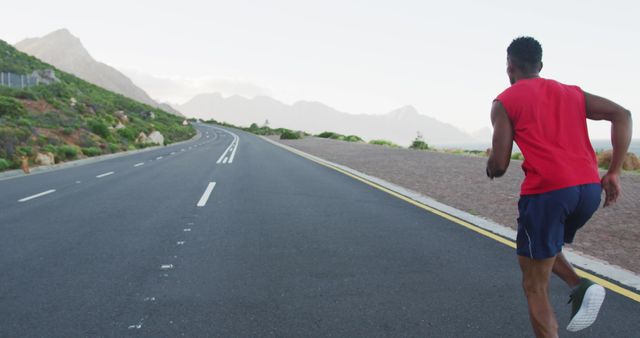 Man running on open road with mountainous landscape. Ideal for themes related to fitness, endurance training, outdoor activities, and health. Perfect for advertisements, fitness blogs, and wellness programs.