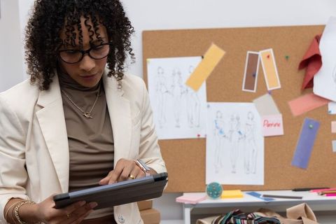 African american fashion designer reviewing tablet with moodboard and fabric swatches in studio