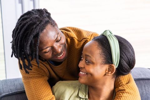 African american couple hugging on couch, smiling and sharing intimate moment
