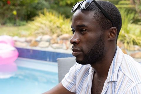 African american man relaxing poolside wearing sunglasses and striped summer shirt