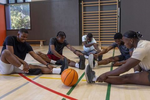 African american basketball players stretching together on indoor court team warmup
