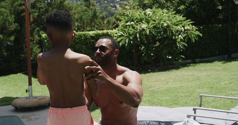 African father applying sunscreen on son poolside protecting skin summer backyard moment