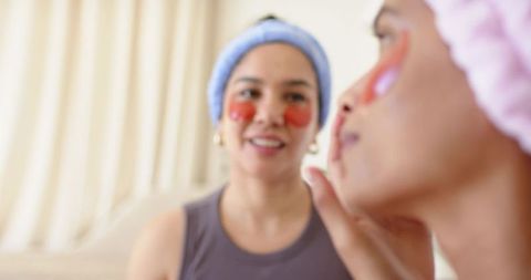 Diverse women relaxing with red hydrogel eye patches doing skincare routine in cozy home