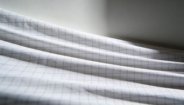 White grid bed sheet draping with soft light and shadowed fabric folds, minimal texture