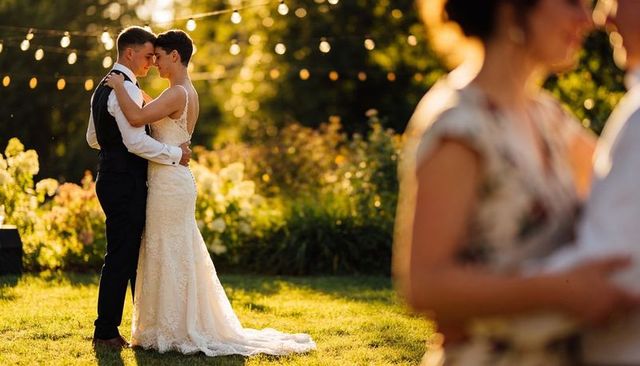 Newlyweds embracing during first dance on garden lawn with string lights at golden hour