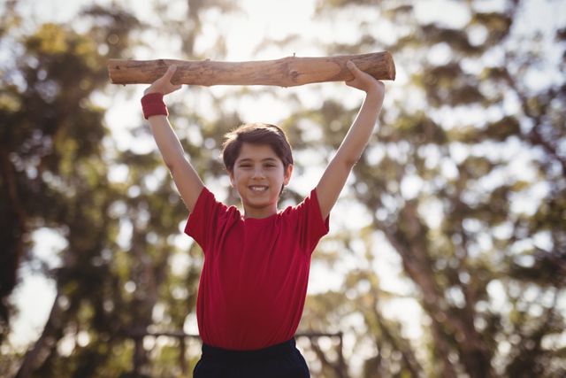 Portrait happy boy exercising with log during obstacle course in boot camp