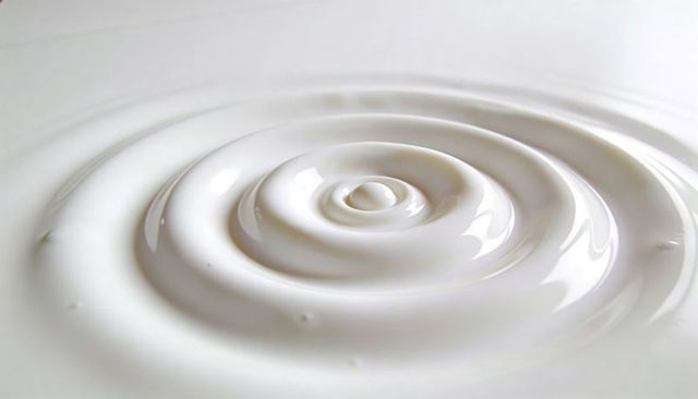 Concentric ripples forming around central droplet in creamy white liquid