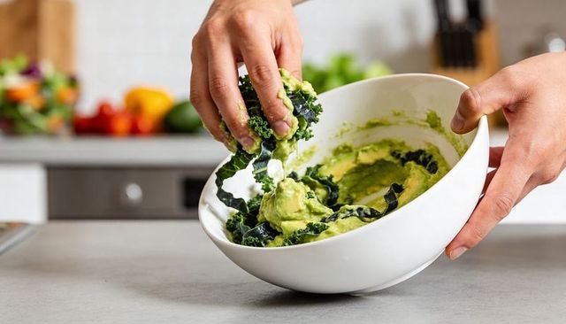 Hands massaging kale into creamy avocado mash for healthy dip or salad