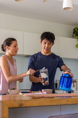 Diverse couple preparing berry yogurt smoothie in modern kitchen, blending breakfast