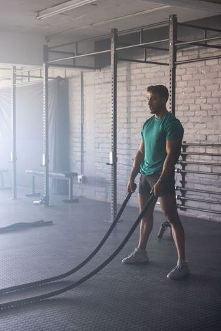 Muscular man training with battle ropes at gym