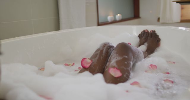 Legs of african american attractive woman taking bath with foam and rose petals. beauty, pampering, home spa and wellbeing concept.