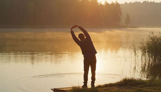 Man stretching at misty lakeside dock during golden sunrise backlit silhouette
