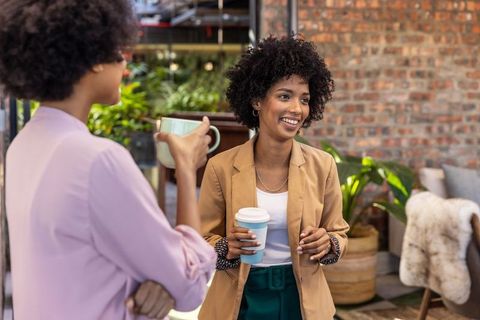 Diverse women chatting in modern office lounge with coffee cups