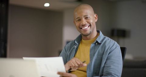 African American man smiling while reviewing documents at modern office desk with laptop