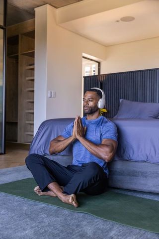 Mature african man practicing seated meditation with headphones in modern bedroom daylight