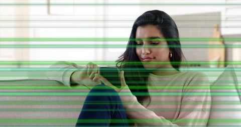 Indian woman using smartphone on sofa with green glitch scan lines for digital disruption