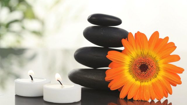 Beautiful composition of spa elements including black stones stacked in a pyramid, an orange flower, and two lit candles. Ideal for promoting spa services, wellness blogs, or relaxation-themed advertisements.