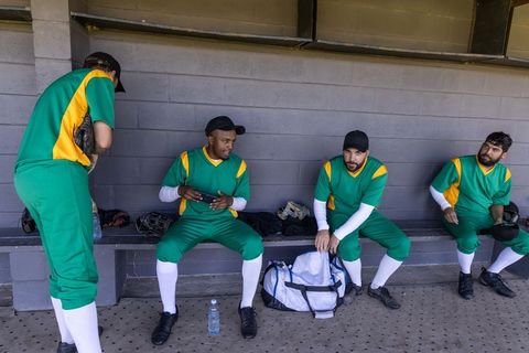 Baseball team sitting in dugout reviewing ar lineup on tablet and planning game strategy