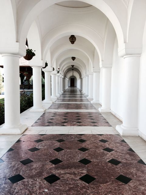 Depicts elegant, white arched corridor with intricate geometric floor tiles. Suitable for use in architectural presentations, historic building projects, interior design showcases, and as a wallpaper for creating a sophisticated atmosphere.