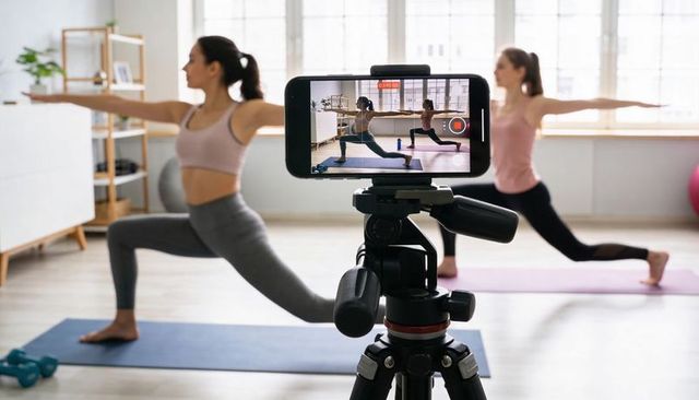 Recording Yoga Class on Smartphone: Two Women Practicing Warrior Pose in Bright Home Studio