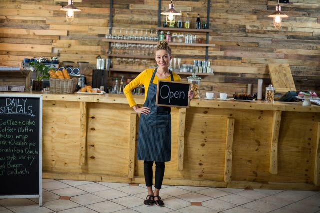 Portrait of smiling waitress standing with open sign board in cafe