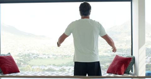 Mature man standing gazing through panoramic window at mountain valley retreat