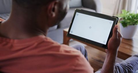 Mature african man holding tablet with target markers for screen mockup in living room