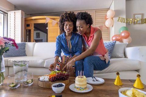 Black women celebrating birthday at home with cake, fruit board, balloons and sash