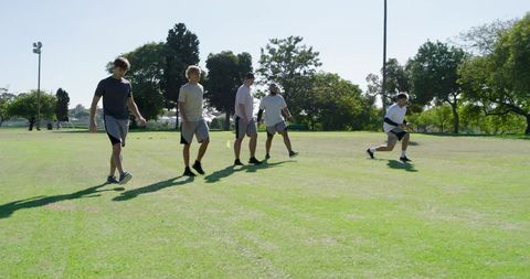 Diverse men performing forward lunges on sunny park field for team fitness training