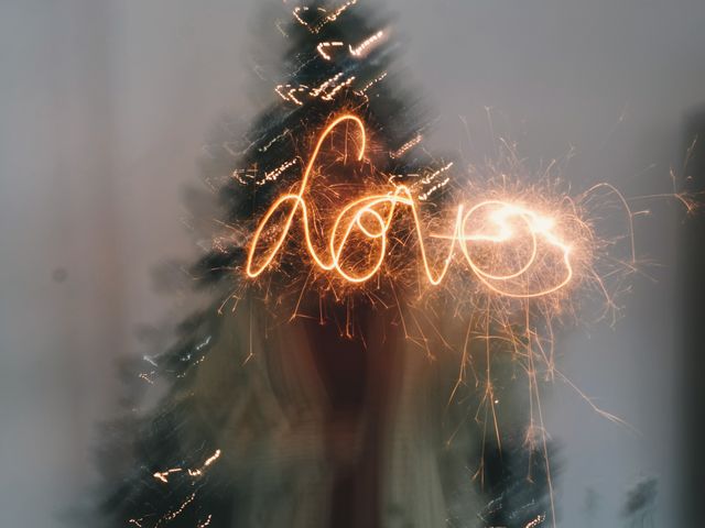 Glowing sparkler trails create the word 'love' in front of beautifully decorated Christmas tree. Blurred effect gives a sense of motion and adds a magical touch. Perfect for holiday greetings, festive advertisements, celebration invitations, and romantic themes.