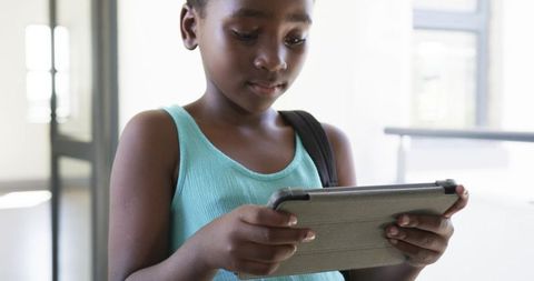 African girl using tablet in sunlit school corridor focusing on learning and technology