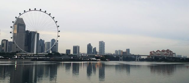 The image captures a panoramic view of Singapore's skyline featuring prominent buildings, a Ferris wheel, and a tranquil waterfront. Ideal for use in travel blogs, tourism websites, urban planning presentations, and promotional materials highlighting modern architecture and city attractions.