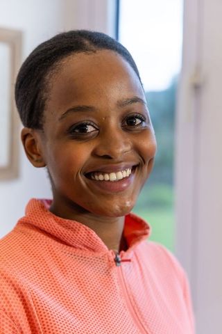 Smiling african american teen in coral textured zip-up jacket near window headshot
