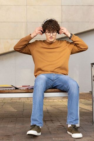 Curly teen adjusting headphones on bench with notebooks urban student lifestyle portrait