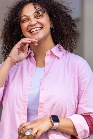 African american woman smiling while holding phone and wearing smartwatch in pink shirt