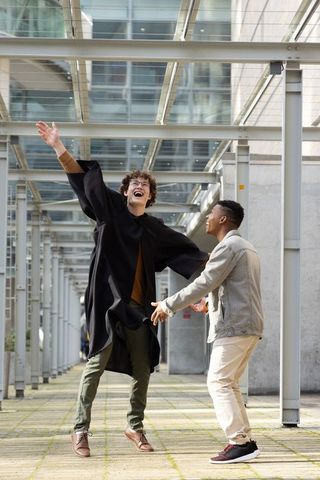Diverse male students celebrating graduation under glass canopy at modern campus walkway