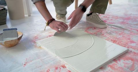 Indian craftsman applying tile adhesive with notched trowel on floor panel