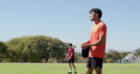Male athlete in bright orange shirt holding towel on sunny grass pitch for team training