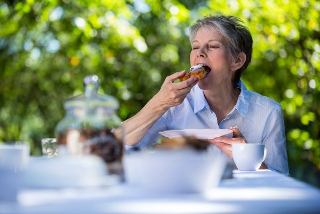 Senior woman eating sweet food in garden on a sunny day