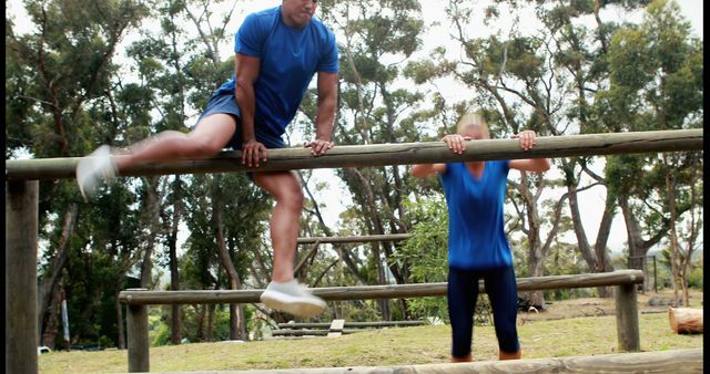 A young African American man is performing a dynamic exercise on parallel bars at an outdoor fitness area, with copy space. A young Caucasian girl is also seen hanging from a lower bar, suggesting a shared workout or family fitness activity.