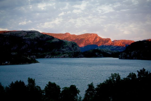 Sunset sunlight bathes the surrounding mountain landscape, reflecting colors off the tranquil lake below. Ideal imagery for travel, nature, and outdoor adventure themes, illustrating peaceful retreats, natural beauty, and breathtaking scenery.